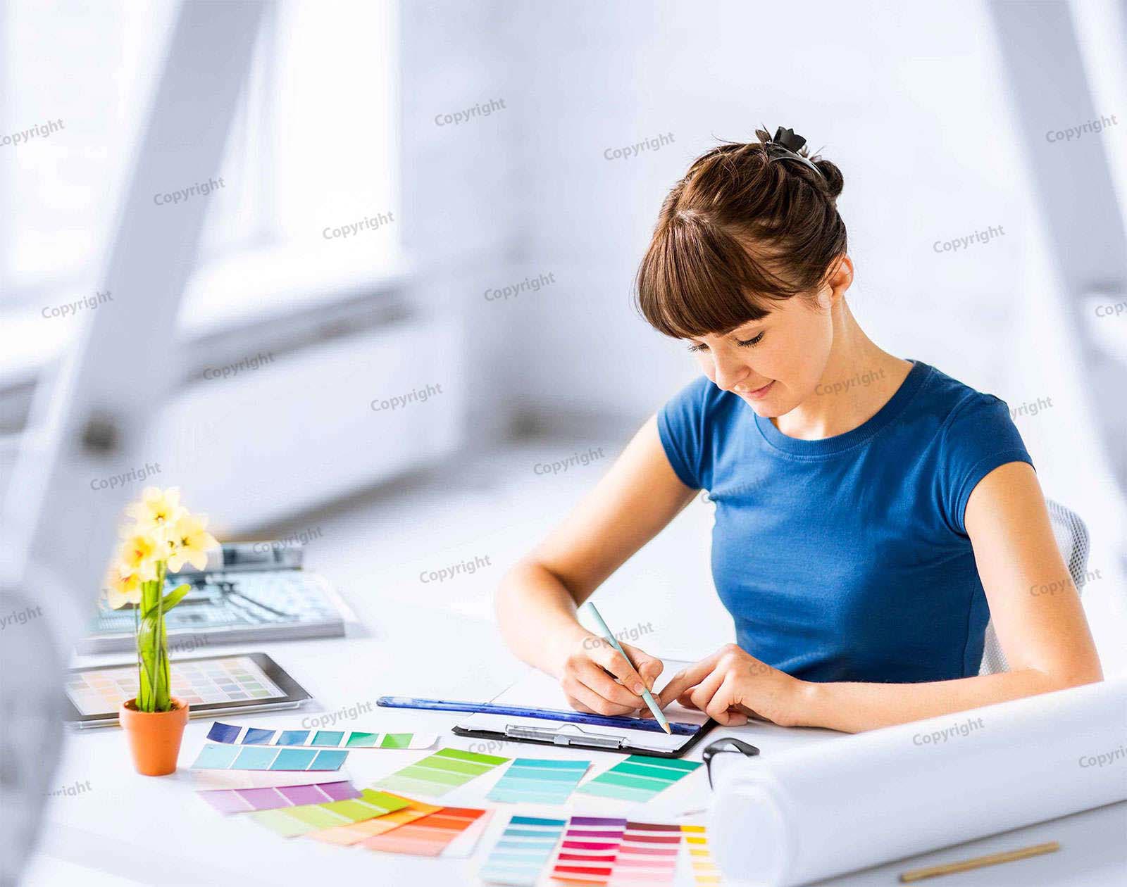 Een vrouw werkt aan een bureau vol kleurstalen en tekent op een vel papier